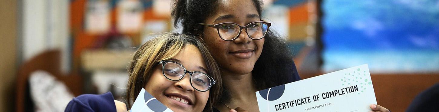 Two students holding their certificates of completion.