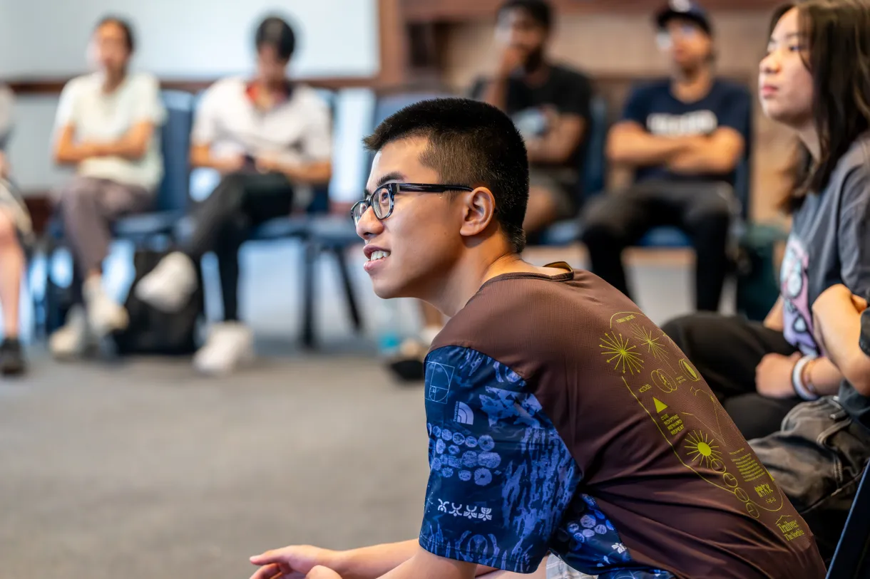 Students seated in a circle, with one student in foreground, smiling and listening